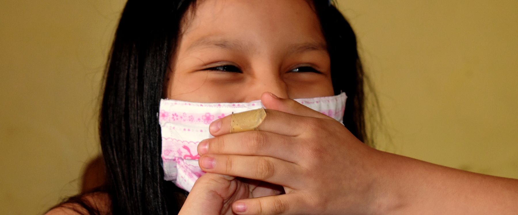 Una niña ríe tapándose la boca con la mano